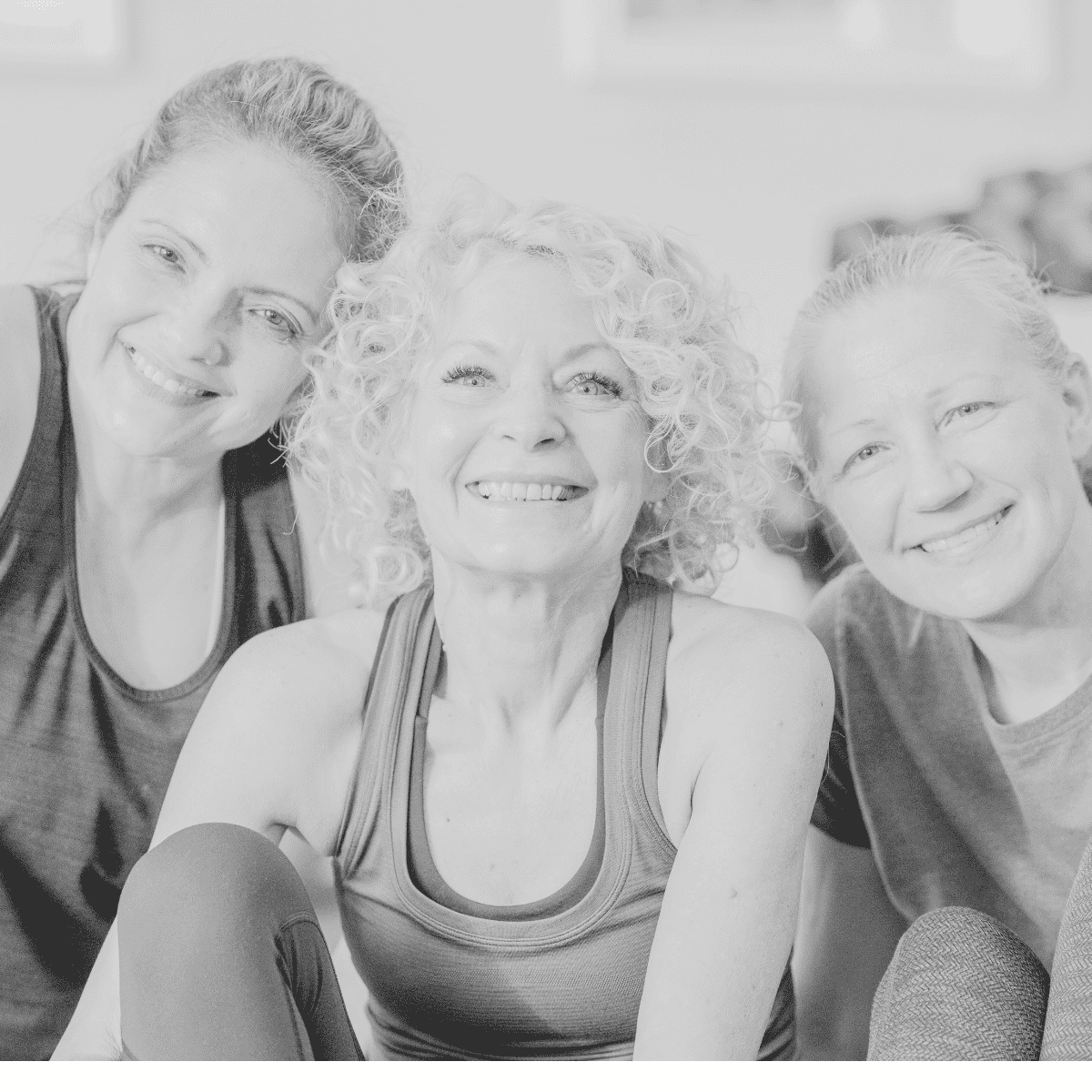 Three smiling women in athletic tops, looking joyful in black and white.