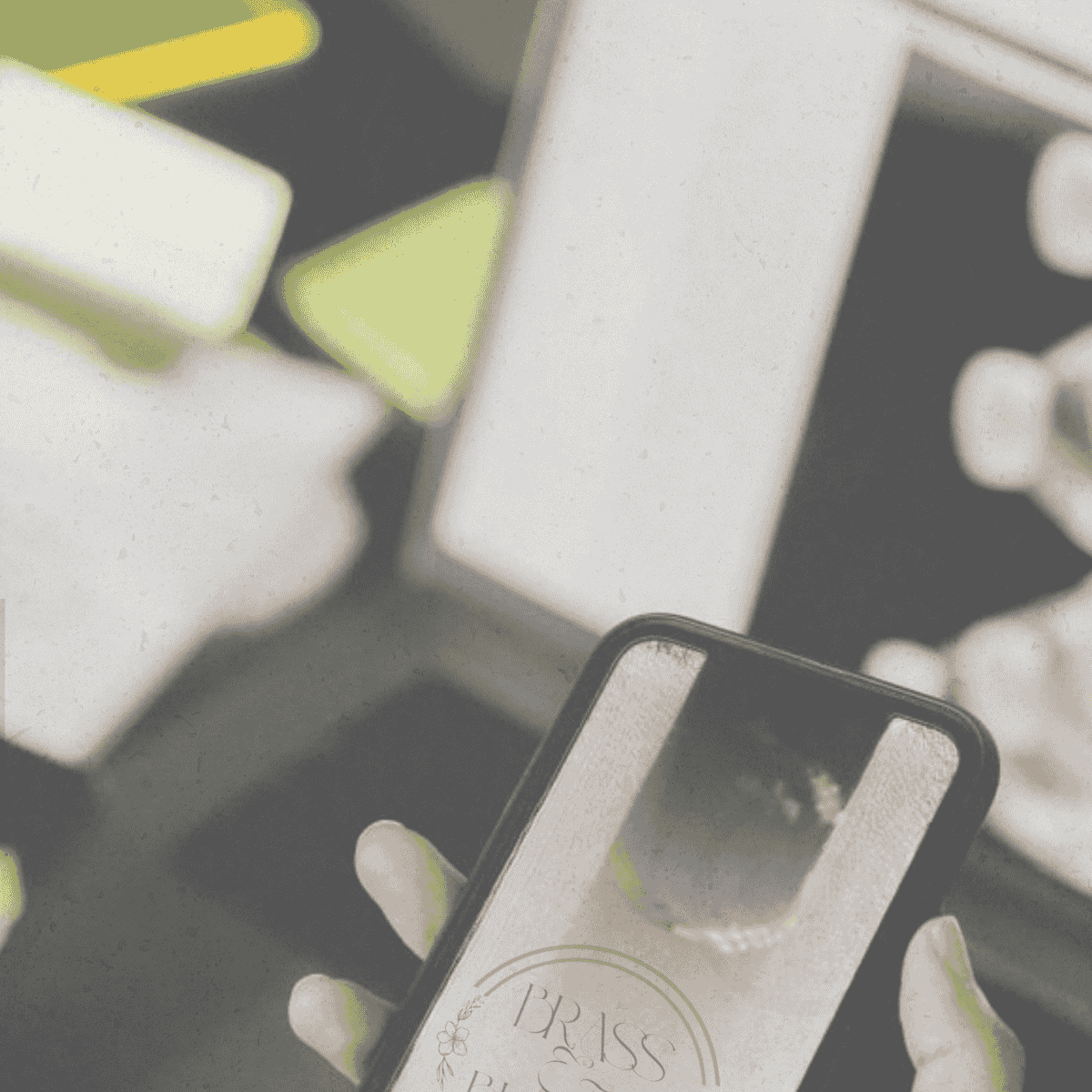 Hand holding a smartphone displaying a "BRASS" logo against a blurred, colorful background.