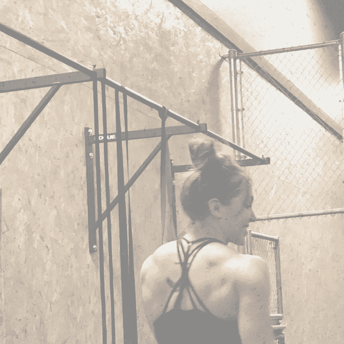 Fit woman with bun, back to camera, looking over shoulder in sepia gym.