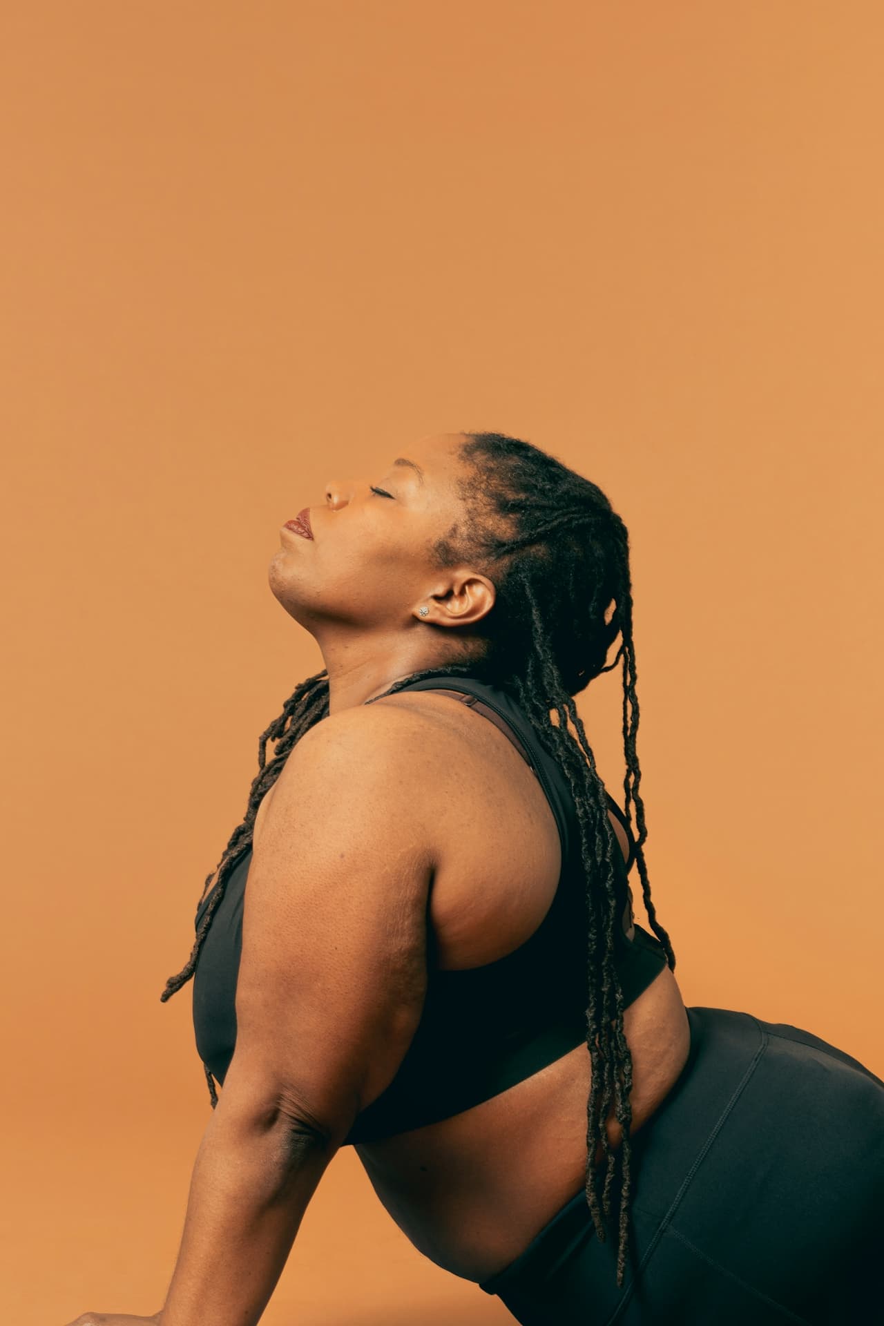 Plus-size Black woman with dreadlocks in yoga pose, head back, eyes closed.